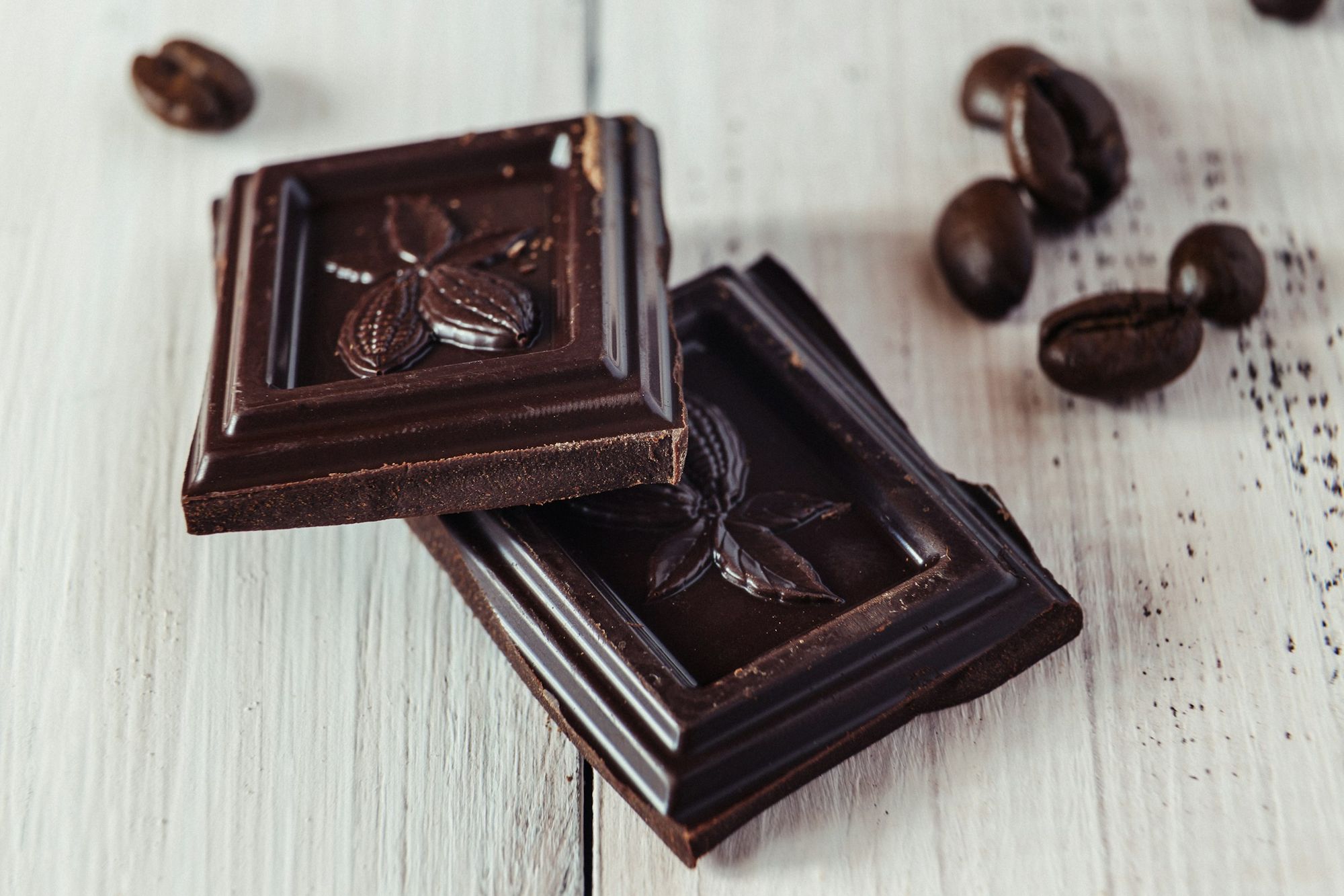 Squares of dark chocolate with coffee beans on a wooden table
